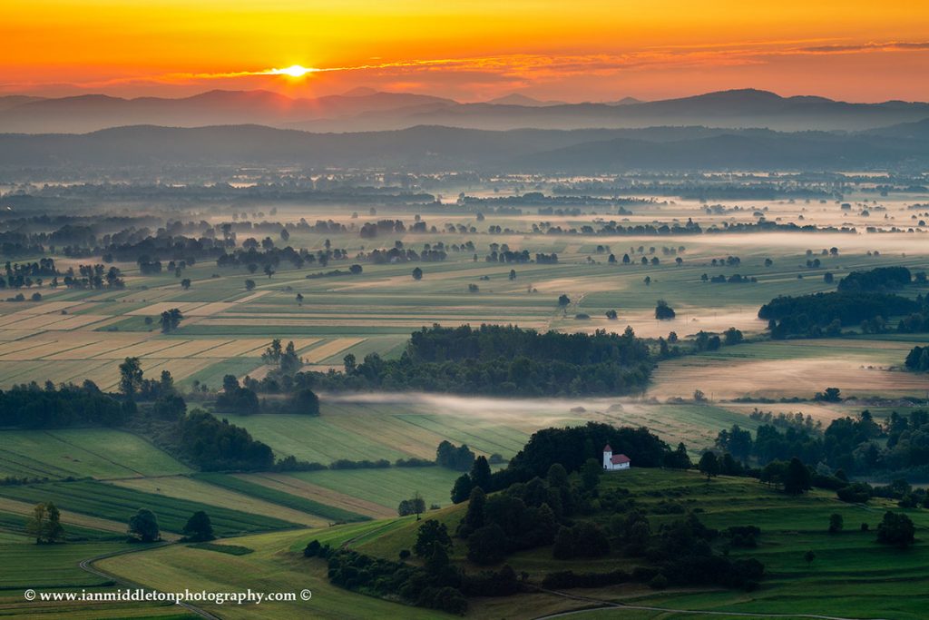 Sunrise over the Ljubljana Marshes and the church of Saint Lawrence, seen from the hilltop church of Sveta Ana in Slovenia.